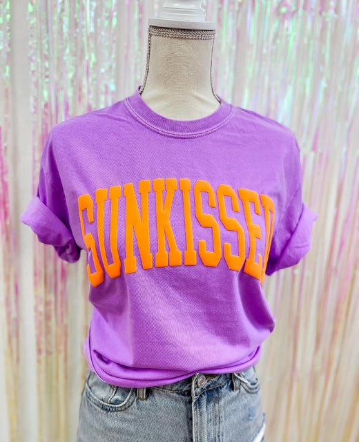 Purple t-shirt with 'SUNKISSED' text on a mannequin against a colorful background